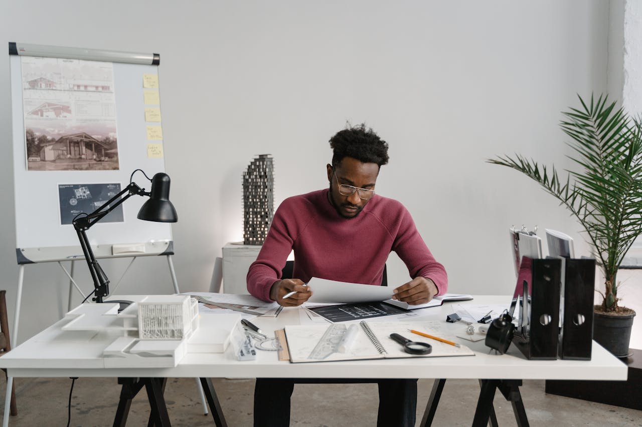 Architect working on designs at a desk cluttered with planning materials and tools.
