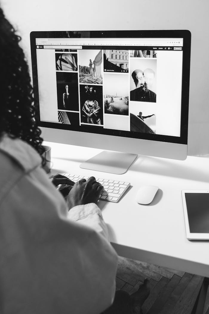 Black and white of crop anonymous African American female working with computer at table with tablet
